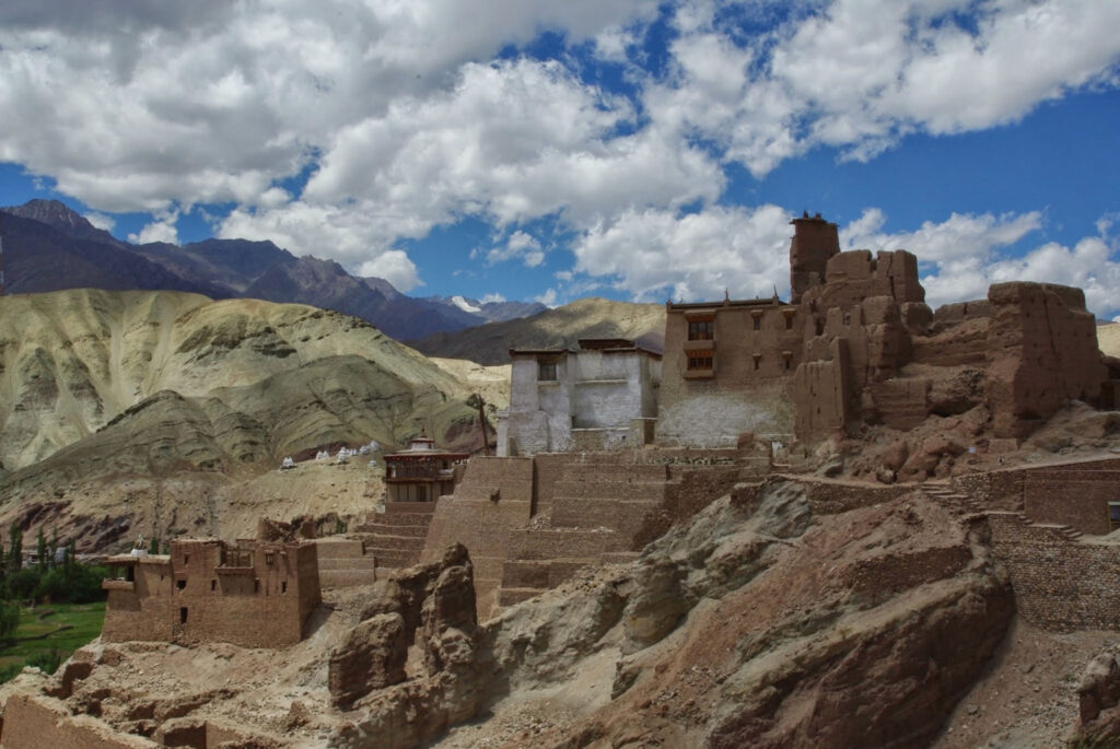 Monastère fortifié en terre et pierre accroché à la montagne, sous un ciel aux nuages sculptés (?)