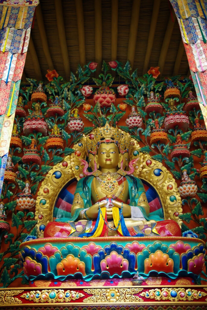 Statue bouddhiste richement ornée et colorée, entourée de motifs floraux et symboliques dans un décor sacré foisonnant