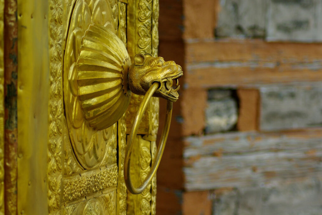 Heurtoir doré sculpté en tête d’animal sur une porte ornée, reflet d’un artisanat riche et symbolique