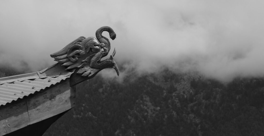 Sculpture de dragon en bois sur un toit face aux montagnes embrumées
