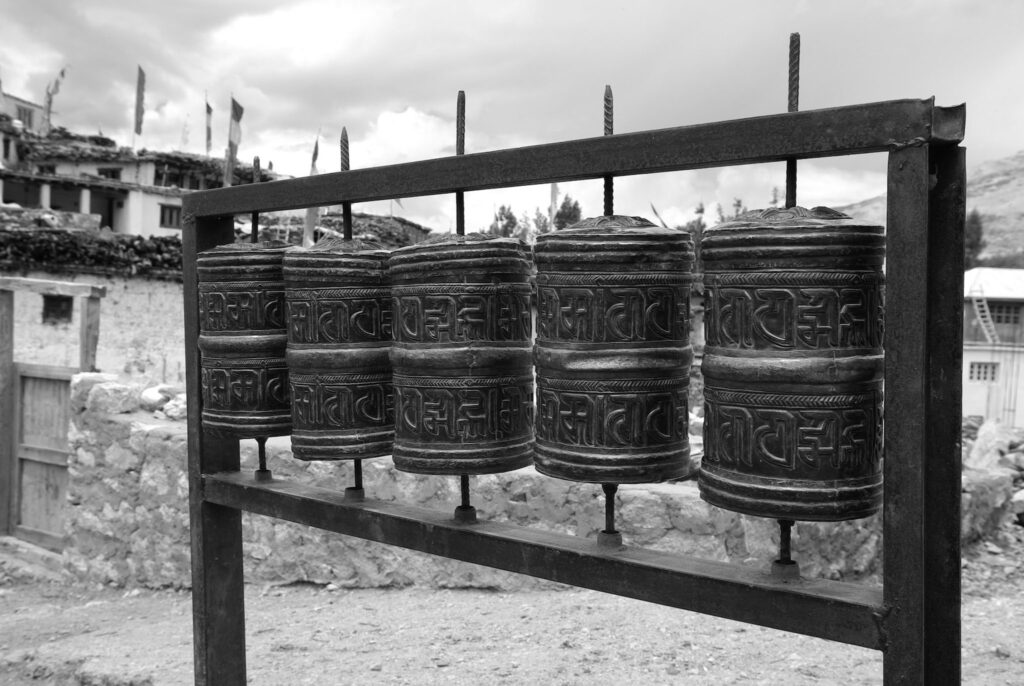 Moulins à prières alignés en métal devant un village de montagne