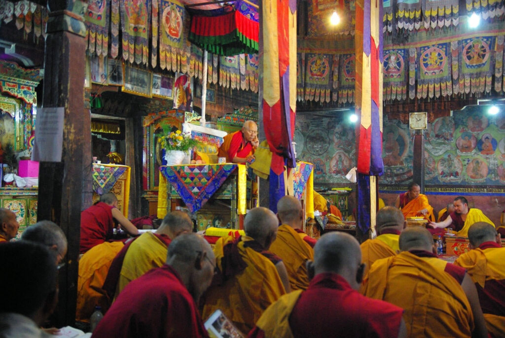 Cérémonie monastique baignée de couleurs et de recueillement, où les moines se rassemblent autour de l’enseignement dans une atmosphère vibrante et sacrée