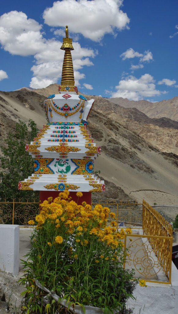 Stupa orné de motifs colorés et de fleurs éclatantes, se dressant avec grâce face aux montagnes minérales et au ciel immense