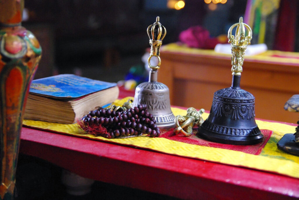 Objets rituels et de méditation posés avec soin, entre clochettes, mala et textes sacrés baignés d’une lumière douce (?)